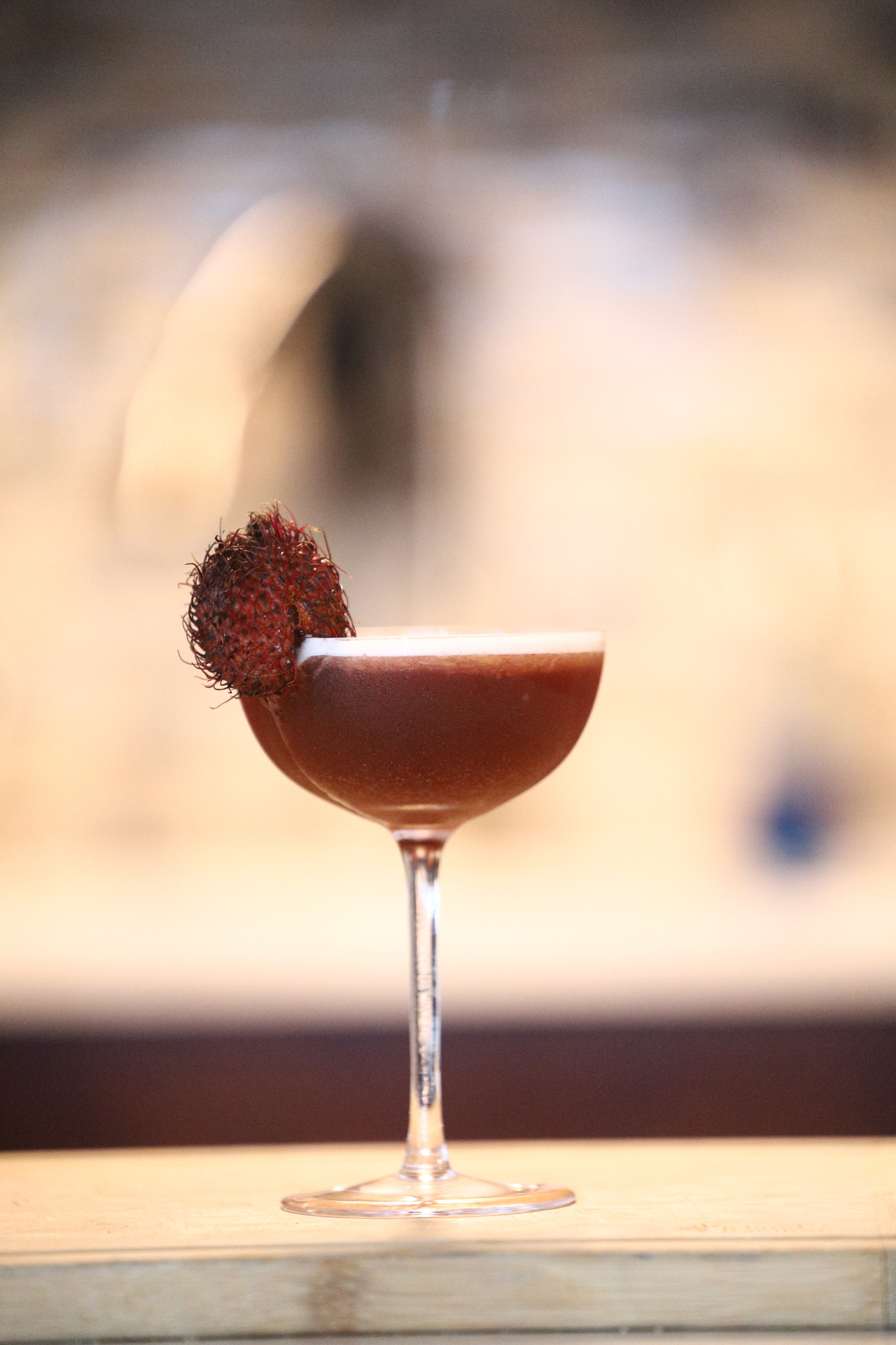 A Drinksbydez signature cocktail — coupe glass garnished with rambutan